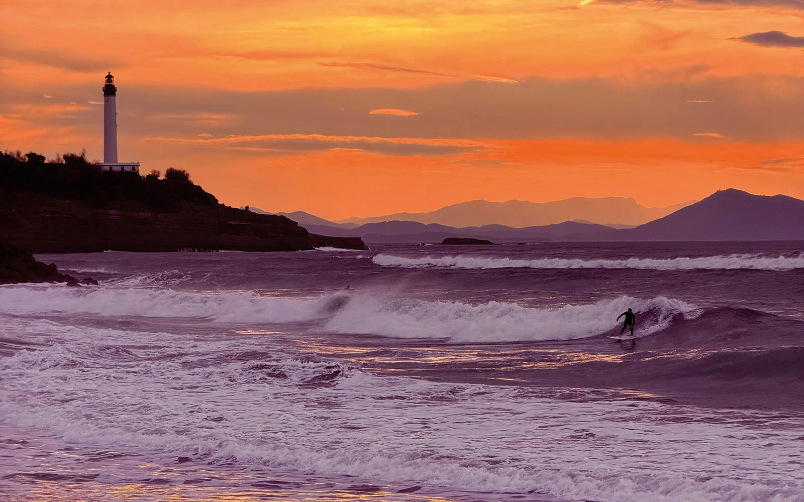 Le phare de Biarritz au coucher de soleil et un surfeur sur la vague — IOcafé, café de spécialité